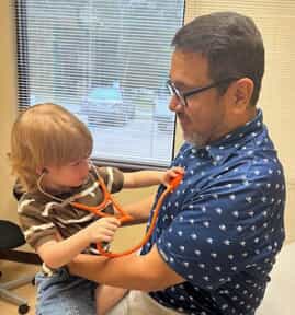 Magdaleno Jacquez III with his young son, who is putting a stethoscope to his chest